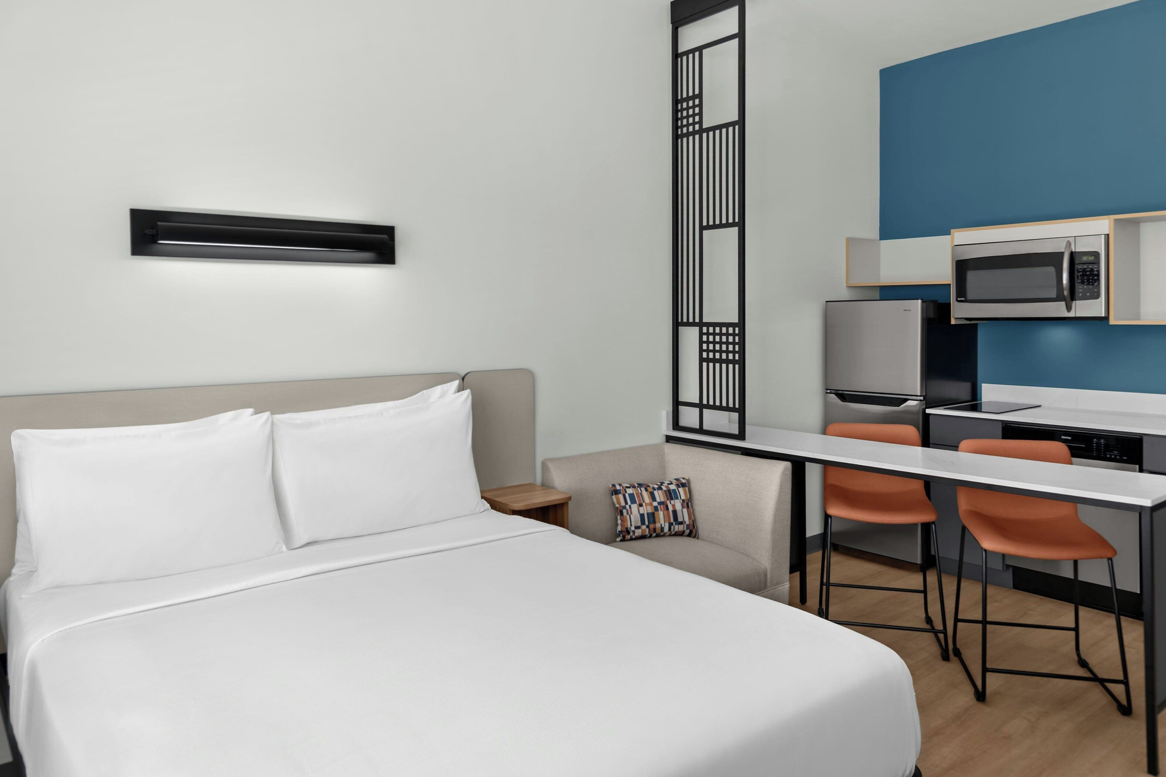 A hotel room with a bed, a desk, a chair, a microwave, and a television.