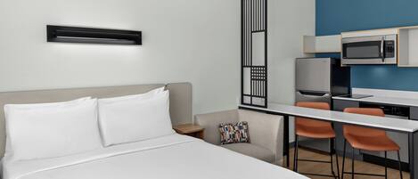 A hotel room with a bed, a desk, a chair, a microwave, and a television.