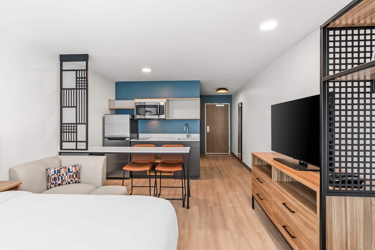 Una habitación de hotel moderna con kitchenette, una cama, un televisor y un comedor.