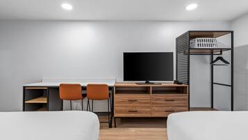 Une chambre moderne équipée d’un lit, d’un bureau, de deux chaises, d’une télévision et d’une armoire.
