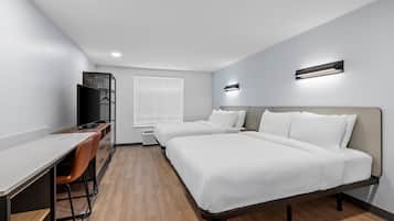 A modern hotel room with a desk, two beds, a TV, and a window with blinds.