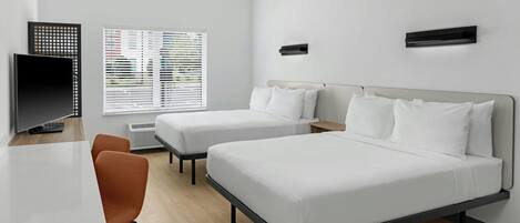 A modern hotel room with two beds, a desk, a chair, and a TV.