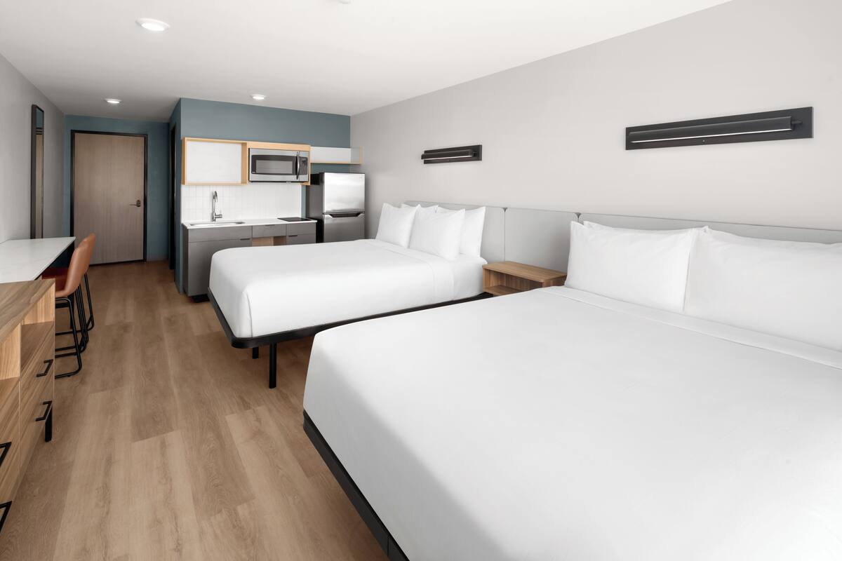 Habitación de hotel con dos camas, un kitchenette, un escritorio y una silla.