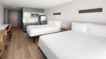 A hotel room with two beds, a kitchenette, a desk, and a chair.