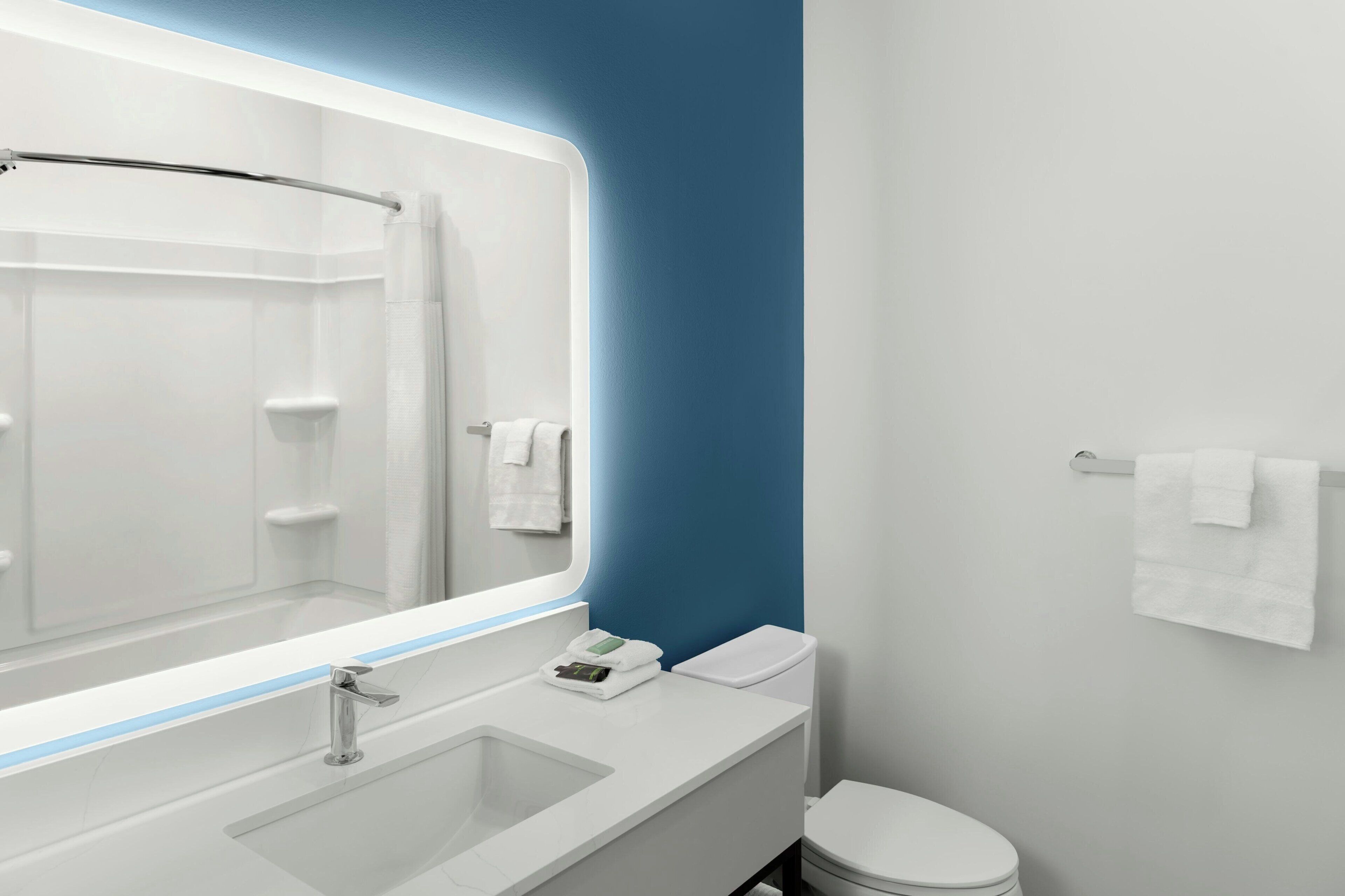 A modern bathroom with a large mirror, a white sink, and a toilet.