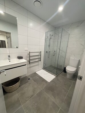 A modern bathroom with a glass shower enclosure, a white sink, and a toilet. - Central Albany, Popular modern 3 Beds +1 Carpark apartment (Auckland)