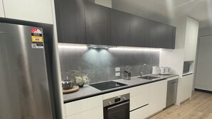 A modern kitchen with stainless steel appliances, a black countertop, and white cabinetry. - Central Albany, Popular modern 3 Beds +1 Carpark apartment (Auckland)