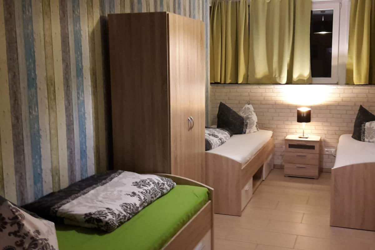 Ein kleines Zimmer mit einem Bett, einem Schrank, einem Nachttisch und einer Lampe.