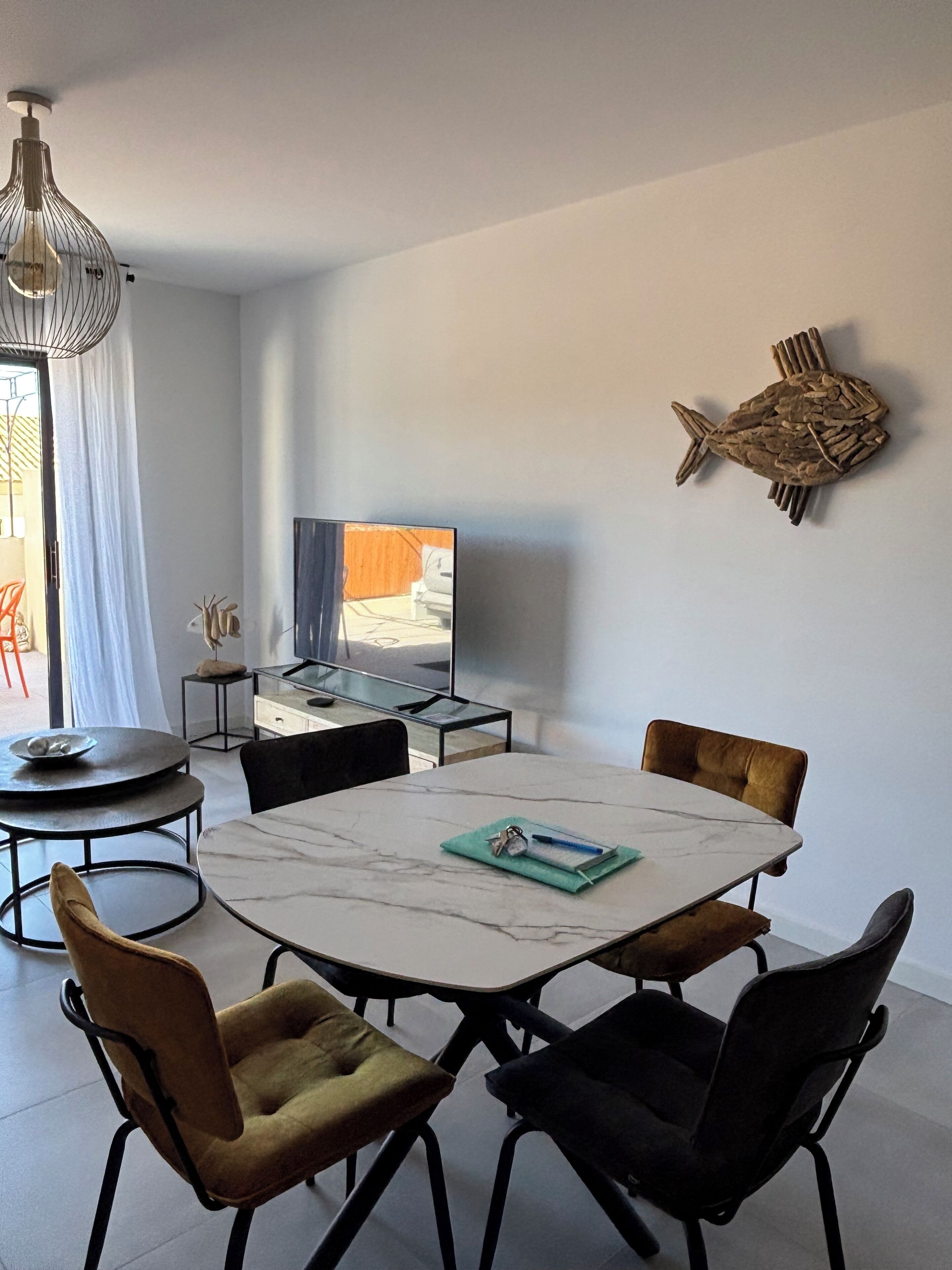 A modern dining area with a marble table, black metal chairs, a television, and a decorative fish wall art piece.