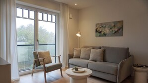 Un salon moderne avec un canapé gris, une chaise en bois, une table basse ronde et un tableau accroché au mur.