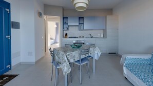 Een kleine leefruimte met een eettafel, stoelen, een bed, een kitchenette en een blauwe deur.