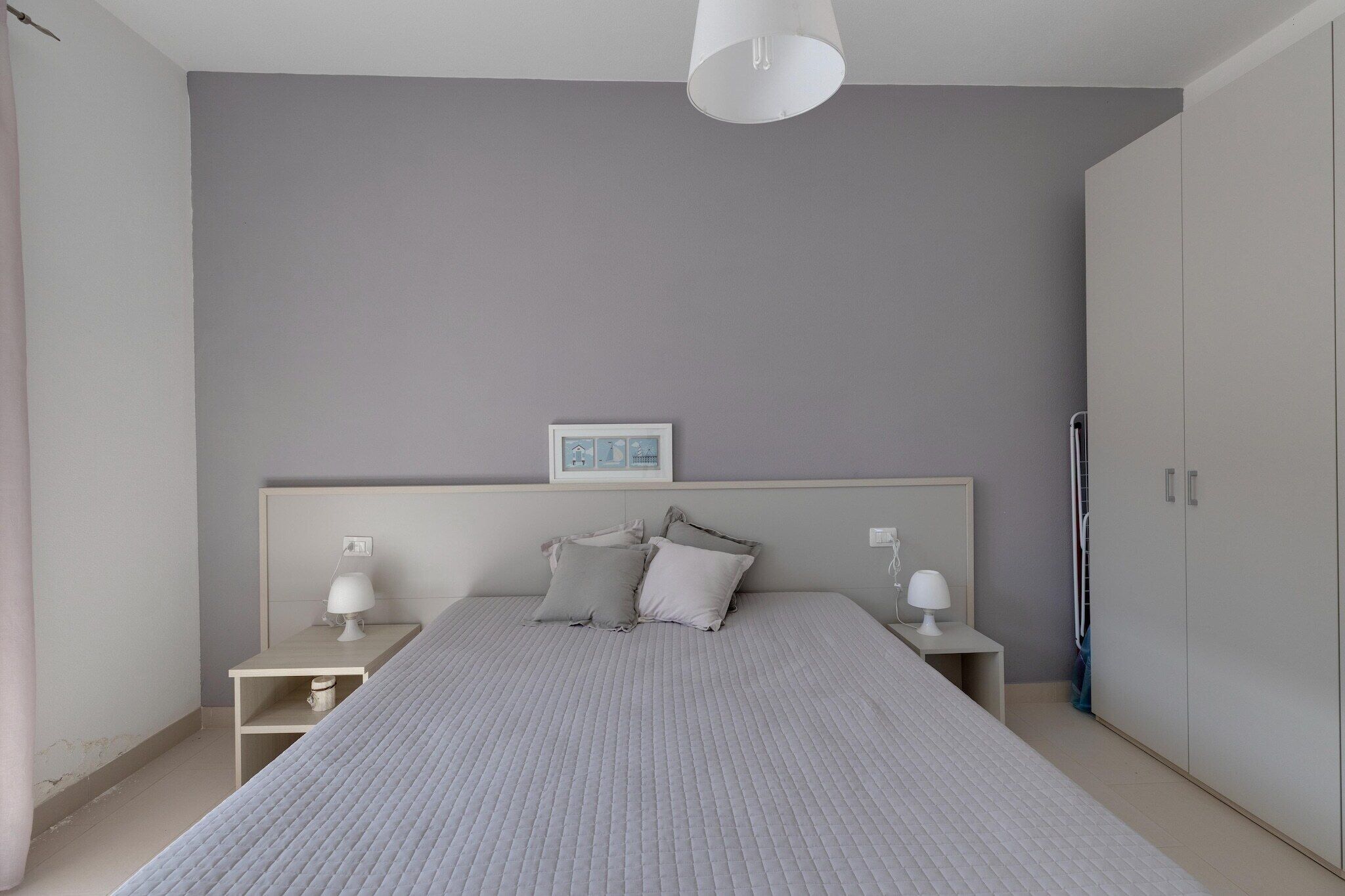 A bedroom with a bed, nightstands, a wardrobe, and a ceiling light.