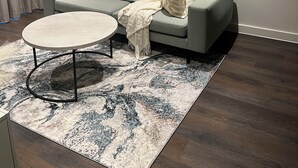 Ein modernes Wohnzimmer mit einem grauen Sofa, einem runden Couchtisch und einem gemusterten Teppich.
