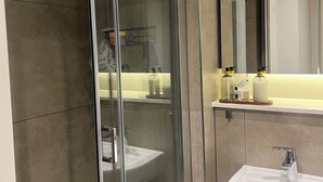 Ein modernes Badezimmer mit einer Duschkabine, einem weißen Waschbecken und einem Spiegel darüber.