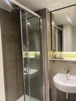A modern bathroom with a glass-enclosed shower, a white sink, and a mirror above it. - Cozy one bedroom in the heart of Birmingham (Birmingham)
