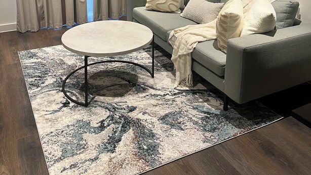 Ein modernes Wohnzimmer mit einem grauen Sofa, einem runden Couchtisch und einem gemusterten Teppich.