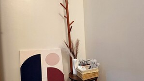 A corner with a wooden coat rack, a framed abstract artwork, and a small table with a basket and decorative items.