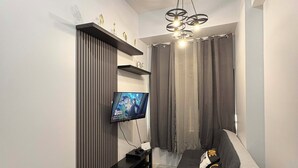 A modern living room with a grey sofa, a flat-screen TV mounted on a wall, a black entertainment unit, and a ceiling fan.
