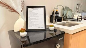 A compact kitchen with a black refrigerator, a framed menu on the counter, and a small potted plant.