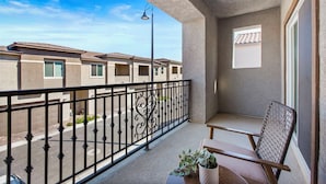 Un balcon doté d’une balustrade en fer forgé, d’une chaise, d’une petite table avec une plante, et offrant une vue sur les immeubles voisins.