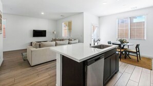 Une cuisine moderne dotée d’un îlot central, un coin repas avec une table ronde et des chaises, et un espace de vie comprenant un canapé et un téléviseur à écran plat.