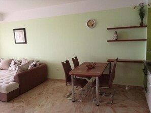 Ein Wohnzimmer mit Sofa, einem Esstisch mit Stühlen, einer Wanduhr und einem Regal mit Dekoration.