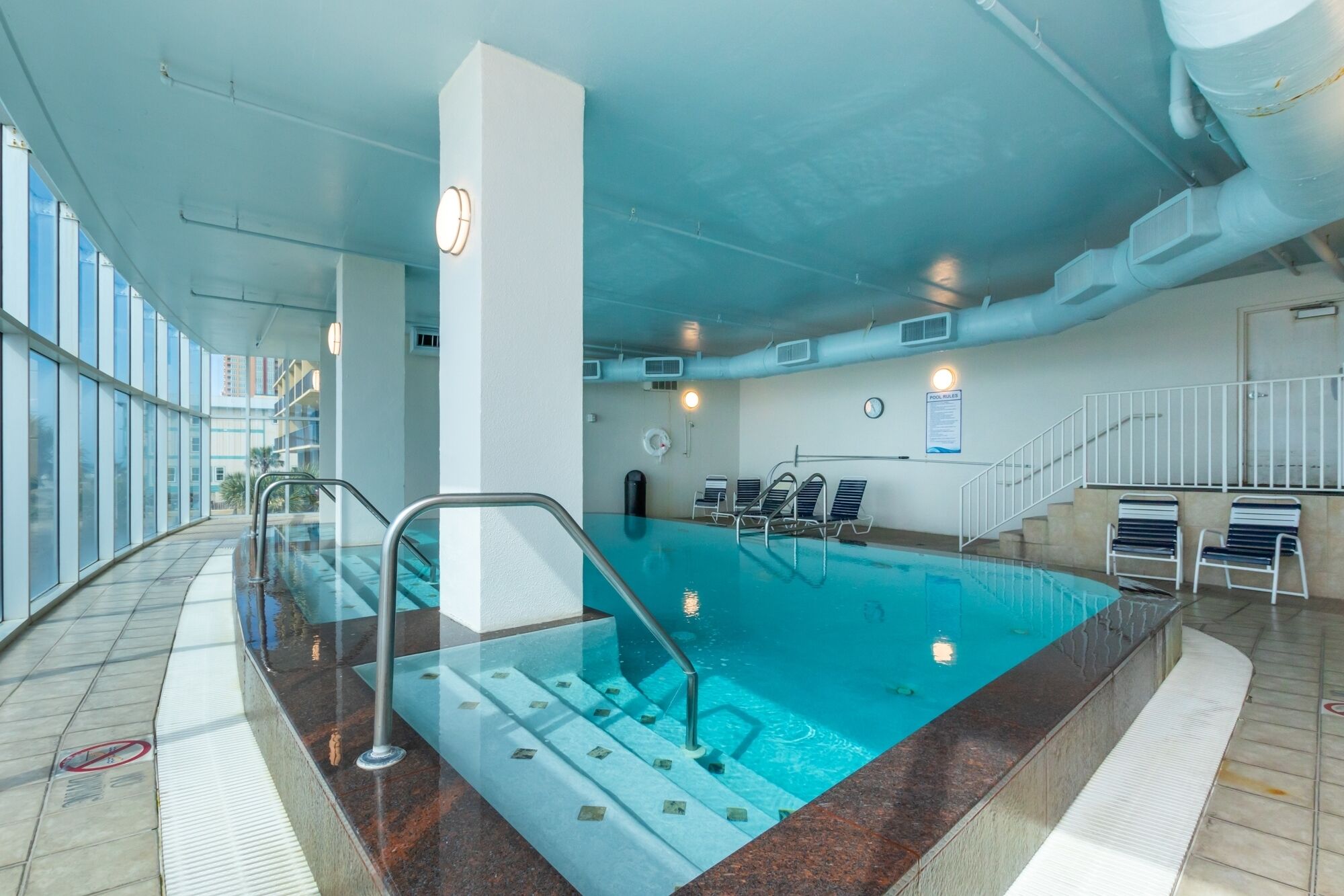 An indoor swimming pool with clear water, a glass barrier, and a few lounge chairs.