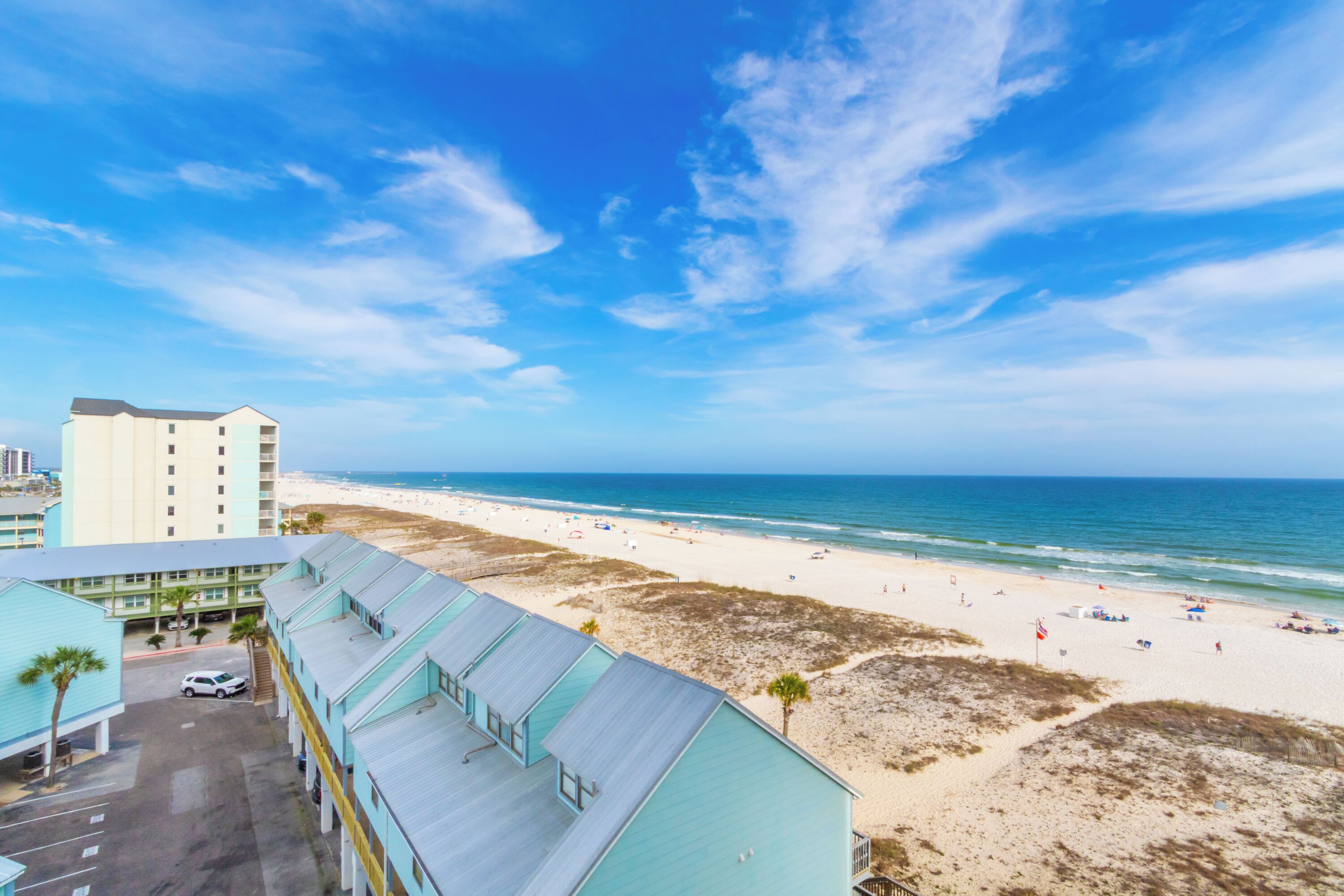 A beachfront hotel with a view of the ocean, a parking lot, and a building with a light blue facade.