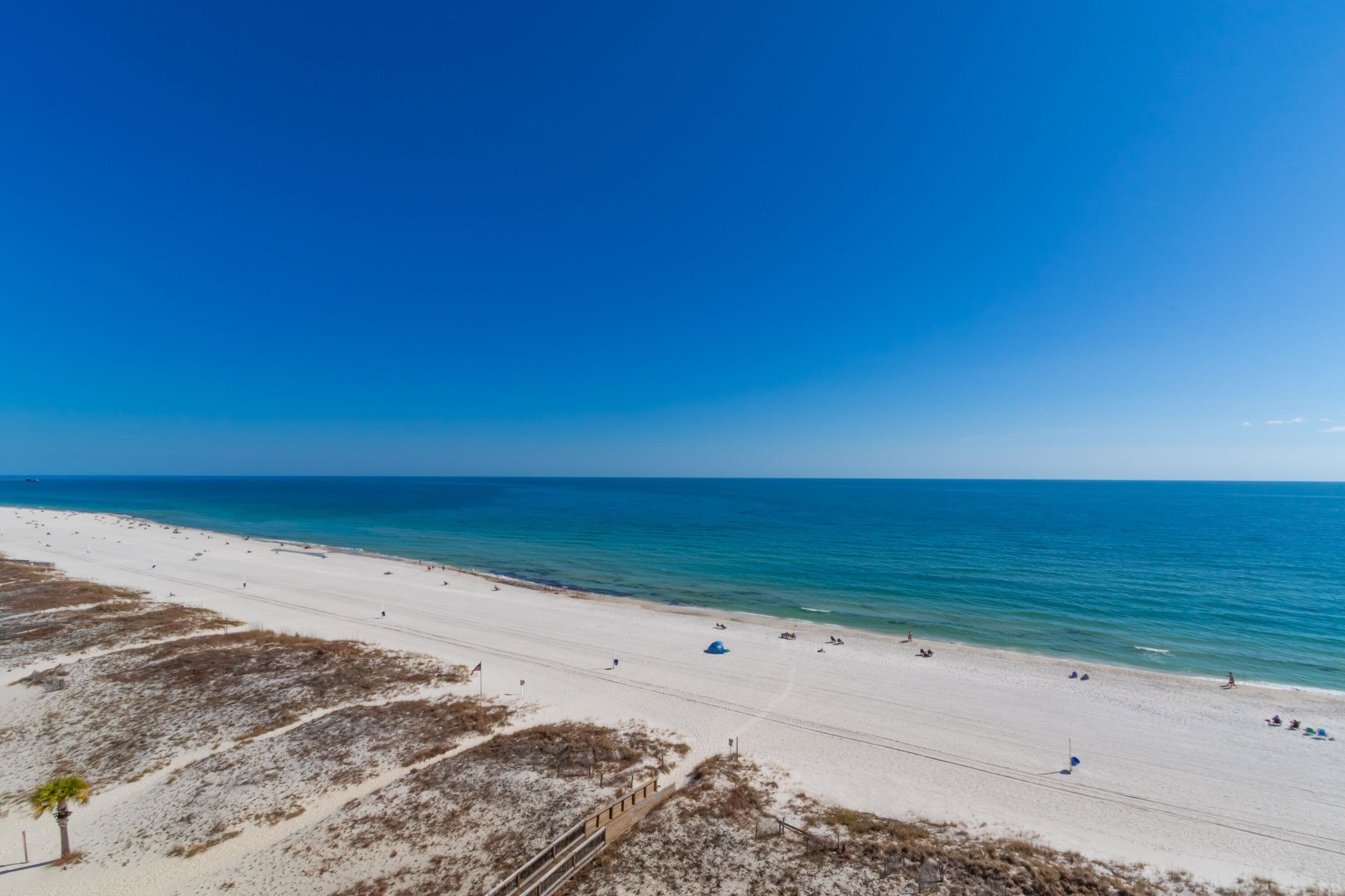 Ein Strand mit blauem Himmel, sandigem Ufer und einigen Personen.