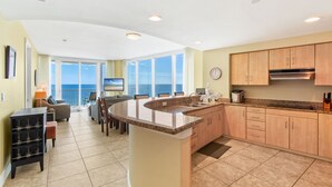 A spacious kitchen with a large island, wooden cabinets, and a view of the ocean through large windows. - Island Tower Condos (Gulf Shores)