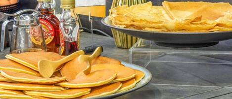 A breakfast buffet with pancakes, crepes, and syrup bottles.