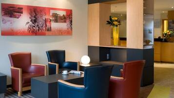 A modern hotel lobby with a seating area, a large abstract painting, and a vase with flowers.