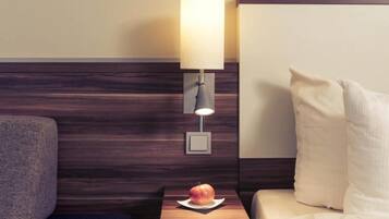 A hotel room with a wooden headboard, a bedside table with a lamp, a pillow, and an apple on the table.