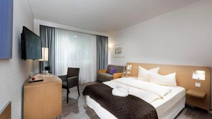 A hotel room with a bed, a desk, a chair, a TV, and a window with curtains. - Sunday Saarbruecken Sued Deluxe Double Room (Saarbrücken)