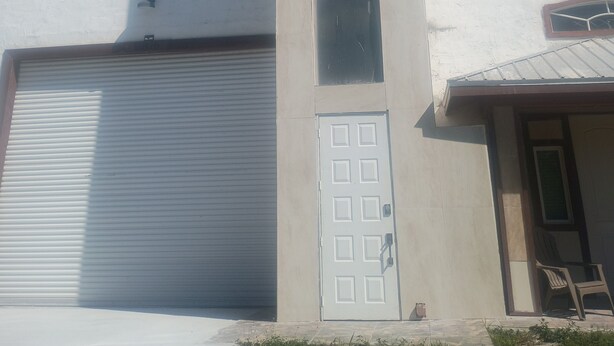 Un edificio con una puerta de garaje, un muro alto con ventanas y una puerta con teclado numérico.