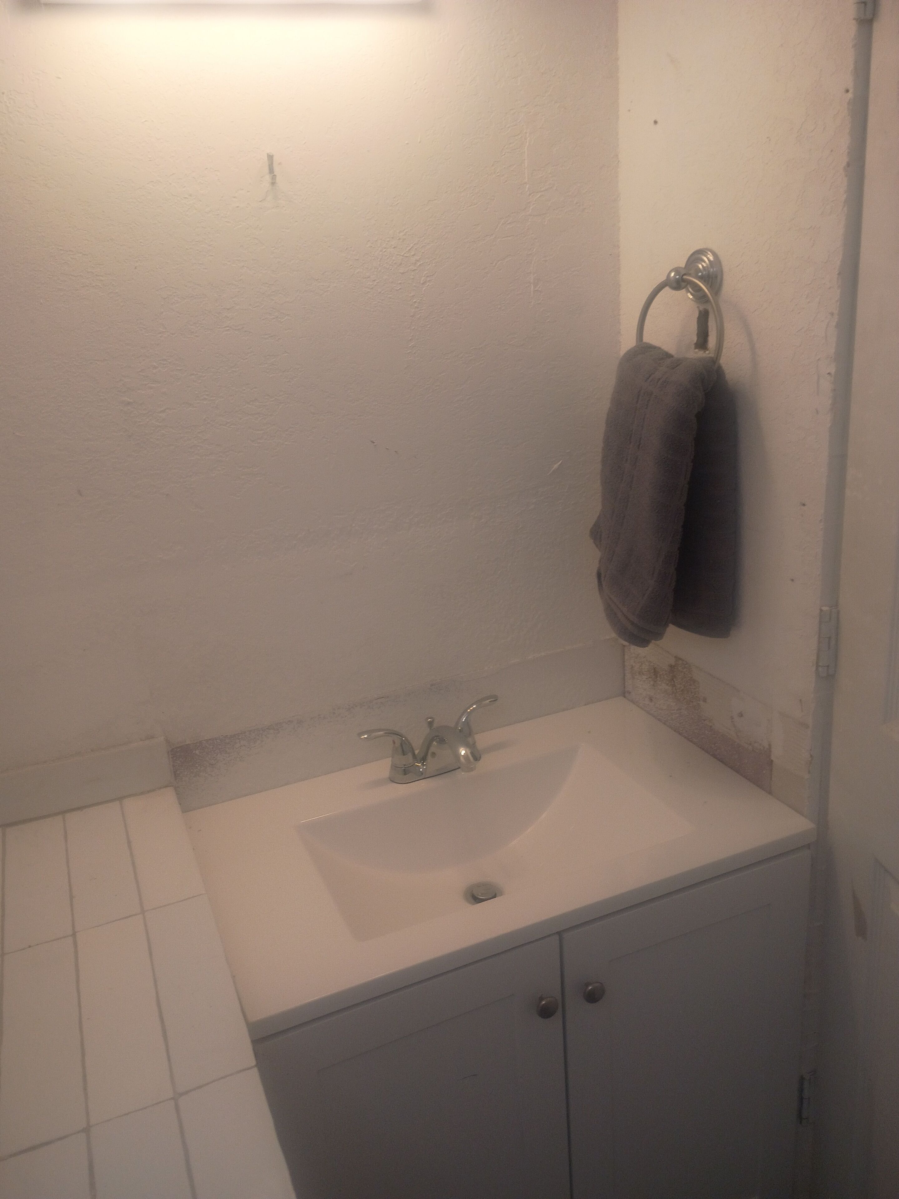 Een badkamer met een witte wastafel, een handdoekhouder met twee handdoeken, en een kastje onder de wastafel.