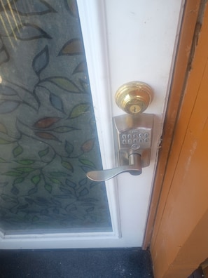 A door with a glass panel featuring a leaf pattern, a brass door knocker, and a numeric keypad lock.