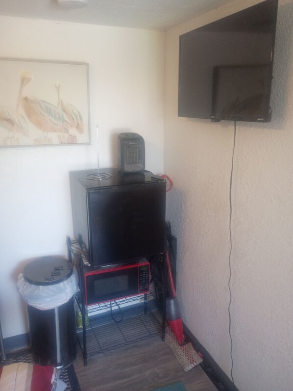 Ein Zimmer mit an der Wand befestigtem Fernseher, einer Mikrowelle und einem Mülleimer.