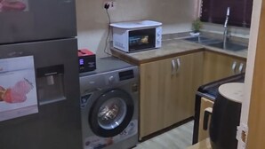 Eine kompakte Küche mit Holzausstattung, einer Waschmaschine, einer Mikrowelle und einem Kühlschrank.