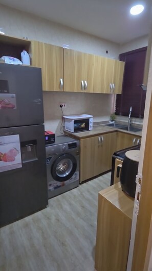 Eine kompakte Küche mit Holzausstattung, einer Waschmaschine, einer Mikrowelle und einem Kühlschrank.