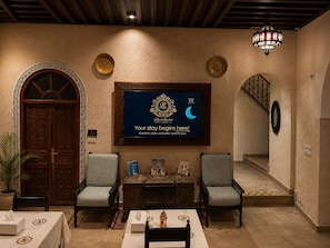 A hotel lobby with a reception desk, two armchairs, a chandelier, and a framed welcome sign. - Riad Zyna (Meknès)