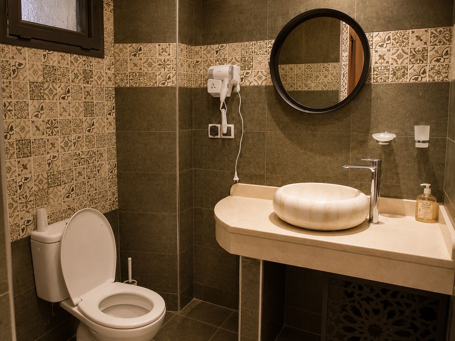 A bathroom with a toilet, sink, mirror, and a hairdryer on the wall.