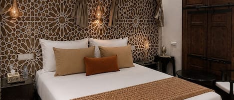A hotel room with a large bed, two bedside tables, a wardrobe, and decorative wall patterns.