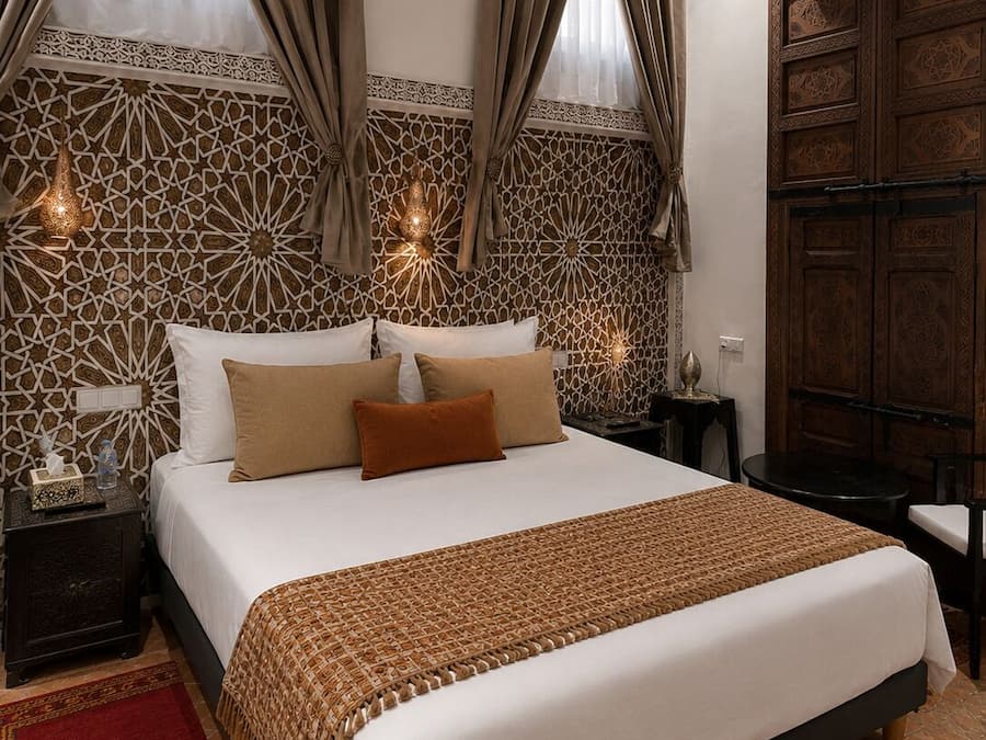 A hotel room with a large bed, two bedside tables, a wardrobe, and decorative wall patterns.