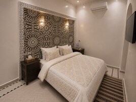 Quarto de hotel com cama, mesas de cabeceira, TV na parede e cabeceira decorativa.