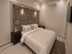 A hotel room with a bed, nightstands, a wall-mounted TV, and a decorative headboard.