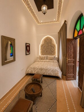A bedroom with a bed, a mirror, a small table, and a decorative wall.
