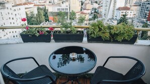 Un balcón con una mesa redonda y dos sillas, con vista a un paisaje urbano con edificios y zonas verdes.