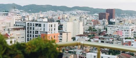 A balcony with a view of a cityscape, including various buildings and a distant mountain range.