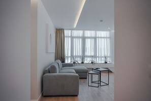Una sala de estar moderna con un sofá seccional gris, una mesita negra y ventanas amplias con cortinas traslúcidas.